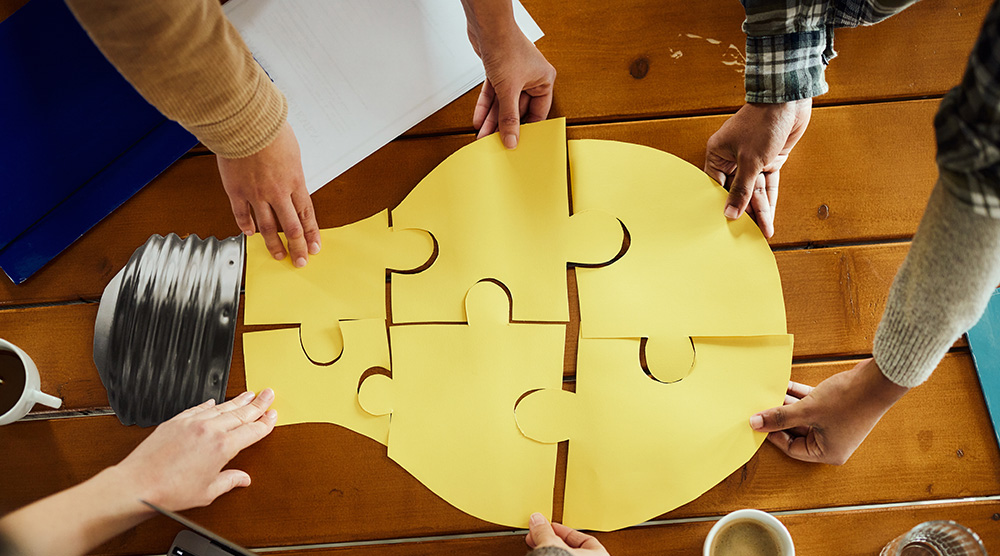 A group of people putting together a puzzle in the shape of a lightbulb