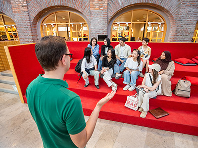 A lecture that speaks in front of students who sit on a red stair. 
